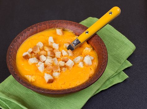 Pumpkin and carrot soup with cream and parsley on dark background