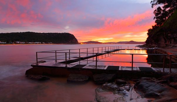 The ocean fed  beach pool located at Pearl Beach, Central Coast of NSW reflecting vivid reds from the glorious sky above at sunrise.