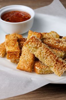 Slices of toast fried in breaded with cheese , sesame and sauce on a paper  in   plate 