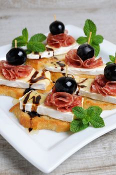 Snack from a toasted slice of baguette with soft under a noble white mold Cheese Brie, salami, a berry of grapes with honey