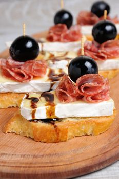 Snack from a toasted slice of baguette with soft under a noble white mold Cheese Brie, salami, a berry of grapes with honey