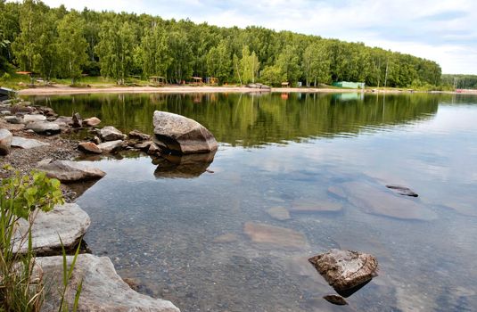 wooded shore of the lake under a cloudy sky