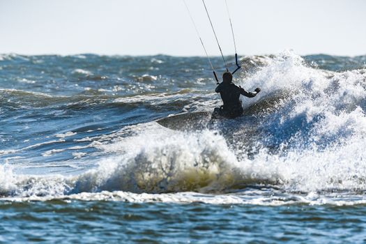 Kitesurfer riding ocean waves on a bright sunny day.