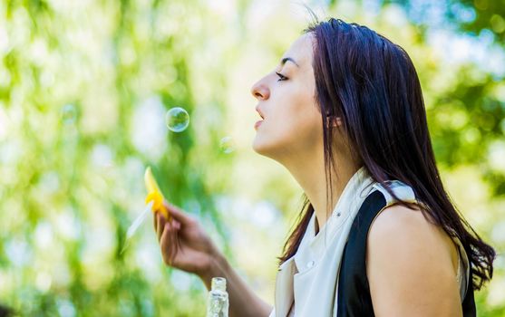 young woman blowing soap bubbles in the park