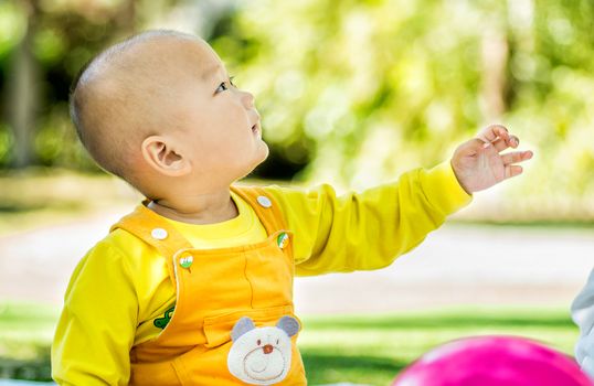 a baby sits on the mat in the park stretching a hand