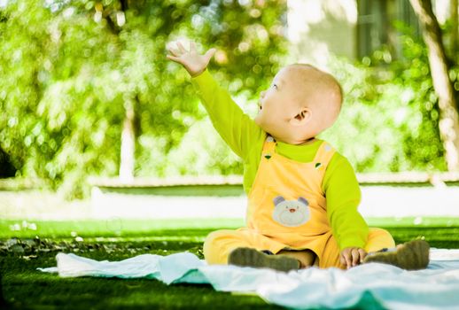 a baby sits on the mat in the park stretching a hand