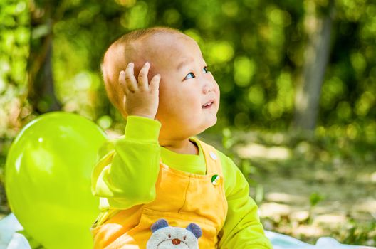 a baby sits on the mat in the park touching his head