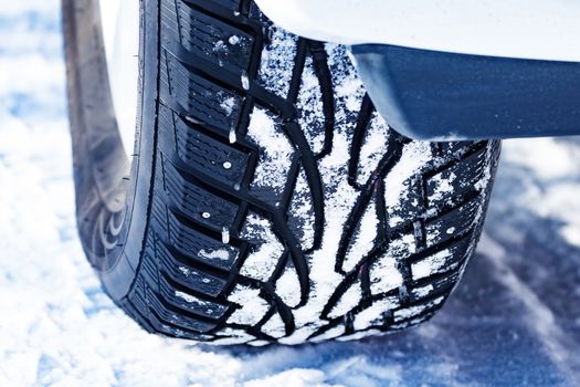 Closeup shot of automobile studded tire covered with snow at winter snowy road