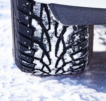 Closeup shot of automobile studded tire covered with snow at winter snowy road