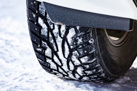 Closeup shot of automobile studded tire covered with snow at winter snowy road