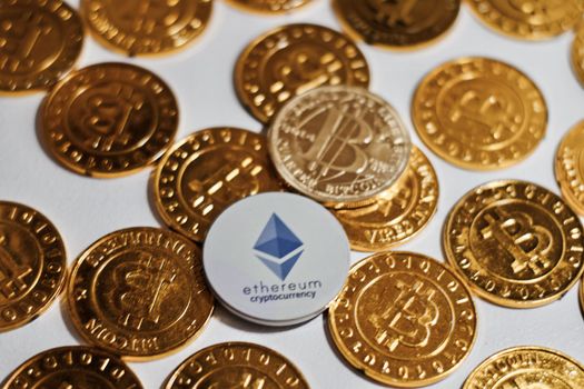 Digital currency physical grey Ethereum coin near gold bitcoins.