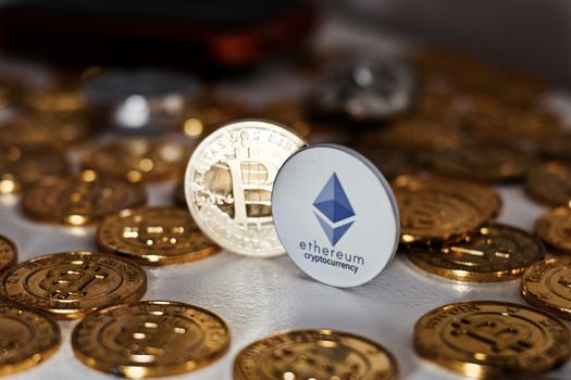 Digital currency physical grey Ethereum coin near gold bitcoins.