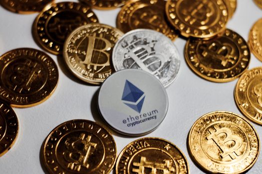 Digital currency physical grey Ethereum coin near gold bitcoins.