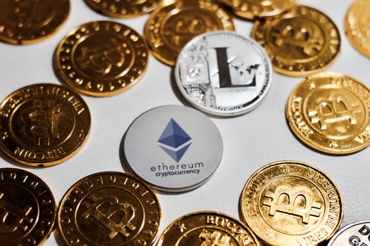 Digital currency physical grey Ethereum coin near gold bitcoins.