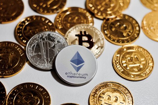Digital currency physical grey Ethereum coin near gold bitcoins.
