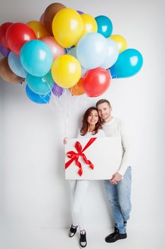 Young smiling couple with balloons and big gift box