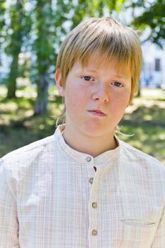 Portrait of serious boy in a white shirt in park