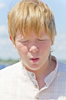 Portrait of squint blond boy in a white shirt near river