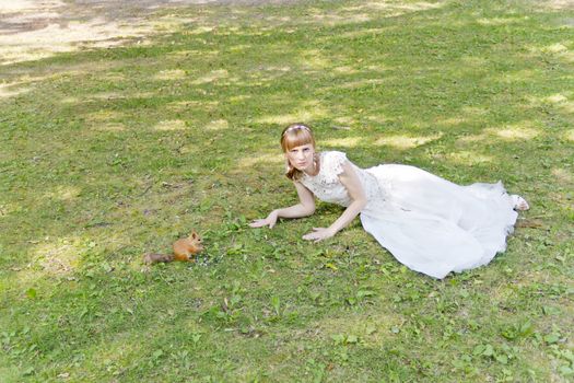 Bride in white lying on grass next to the squirrel in summer