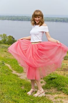 Dancing beautiful girl in pink skirt on river side
