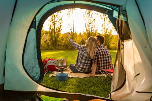 Shot of a happy couple camping on the nature and making a selfie