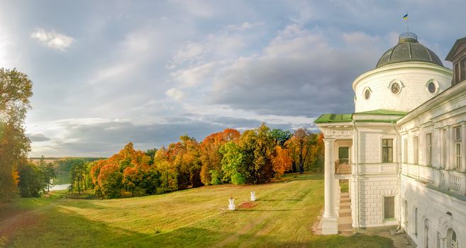 Facade of the 18th century neoclassical palace and large glade in front of him in autumn landscape park on the shore of a pond in national historic cultural preserve Kachanivka, Ukraine
