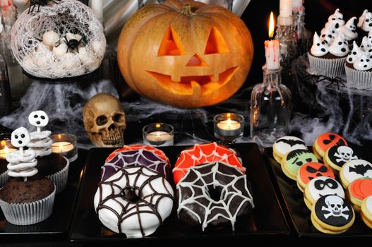 Dishes with glazed donuts, muffins with skeletons, cookies with marzipan on a Halloween table