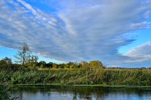 Colorful autumn landscape with a river and clouds.