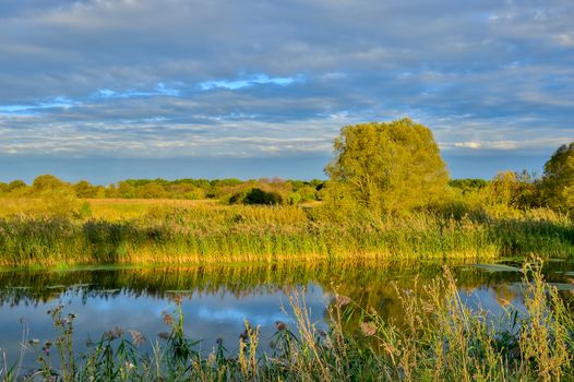 Colorful autumn landscape with a river and clouds.