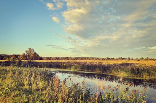 Colorful autumn landscape with a river and clouds.
