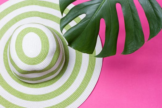 on green monstera leaf with sunglasses and straw hat on pink marble table