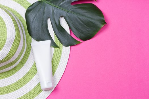 on green monstera leaf with sunglasses and straw hat on pink marble table