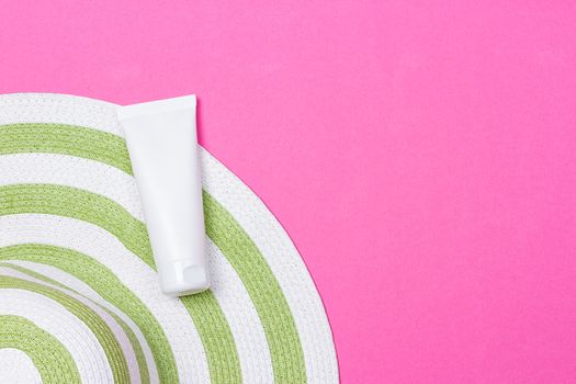 Beach green straw female hat and sun protection cream on a pink background