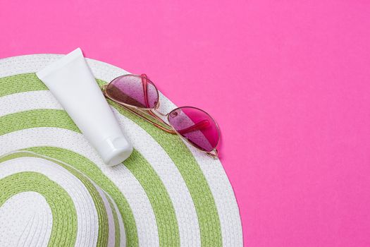 Straw hat and sun block lotion tube and sunglasses on a pink background