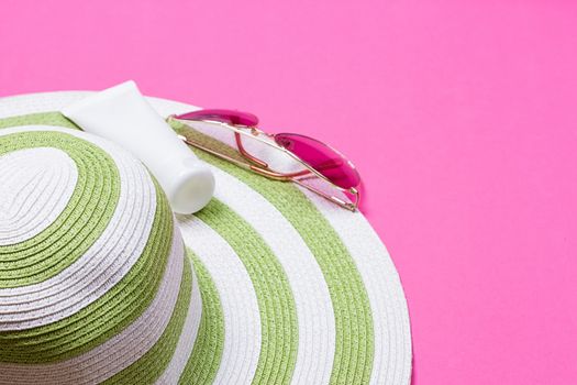 Straw hat and sun block lotion tube and sunglasses on a pink background