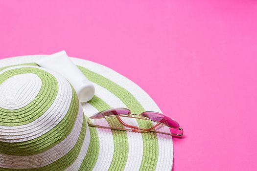 Straw hat and sun block lotion tube and sunglasses on a pink background