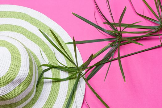 Beach hat and coconut leaves on pink background