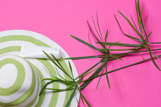 Beach hat and coconut leaves on pink background