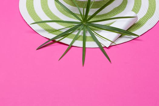 Beach hat and coconut leaves on pink background