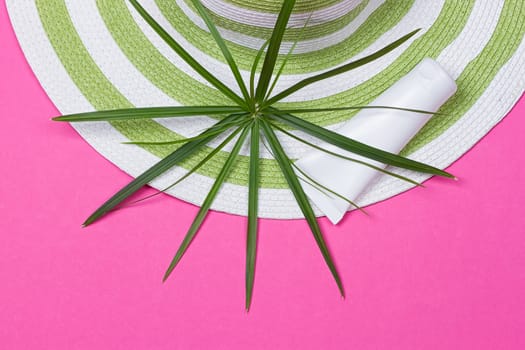 Beach hat and coconut leaves on pink background