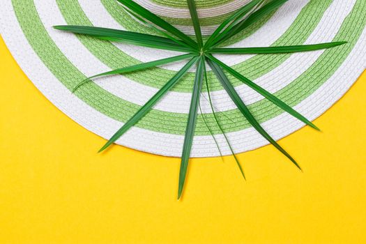 Beach hat and coconut leaves on yellow background