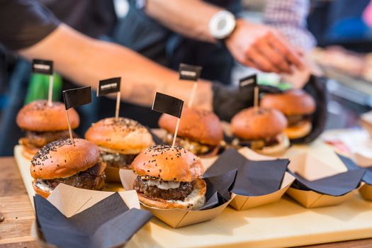 Chef making beef burgers outdoor on open kitchen international food festival event. Street food ready to serve on a food stall.