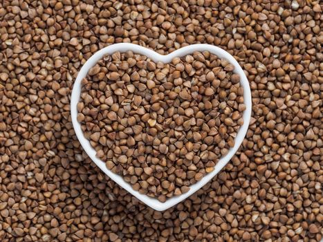 Heart-shaped bowl of roasted buckwheat on gray cement background. Gluten free and healthy diet. I love buckwheat concept. Copy space.
