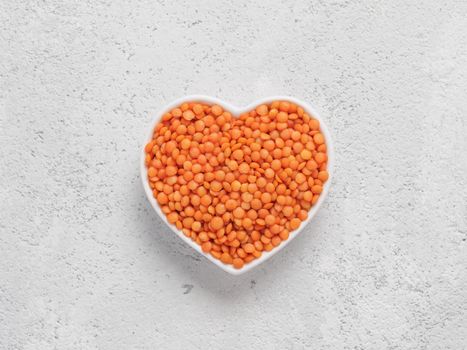 Red orange lentil Football in heart bowl on gray cement background. Copy space. Top view or flat lay.