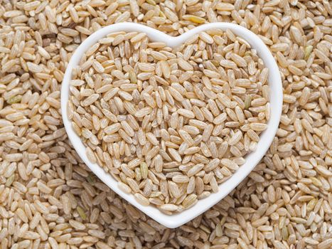 Brown rice in heart-shaped bowl on rice background. Copy space. Top view or flat lay.