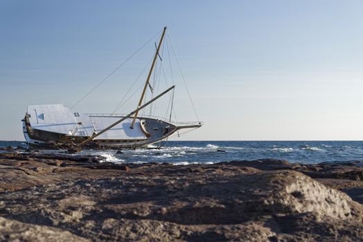 Sailboat, stranded along the coast on the cliff of Sardinia in the Mediterranean Sea.