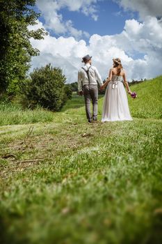 Photo of a young newlywed couple walking down a path through a park holding hands.
