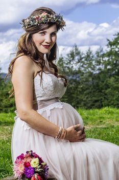 Photo of a gorgeous pregnant bride sitting on a bench waiting for the ceremony to start.