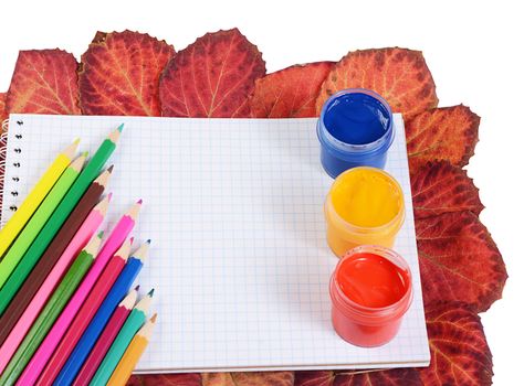 Colored pencils with notebook and autumn leaves