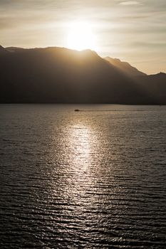 Small boat sailing in the sea at sunset with mountains on background